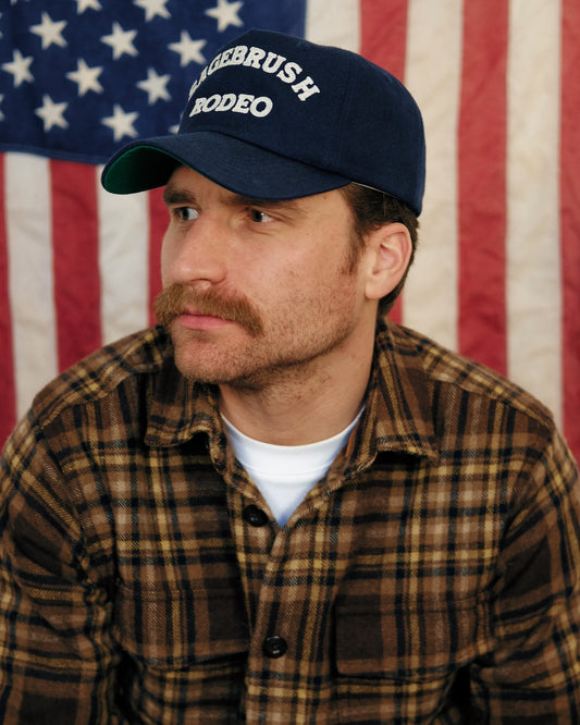 Man wearing a cap with 'Sagebrush Rodeo' text in front of an American flag